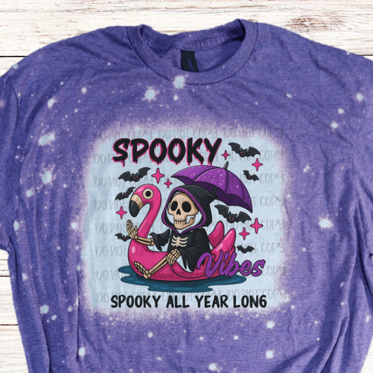 Purple t-shirt with a Halloween-themed design featuring on flamingo water tube and skeleton
